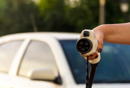 A female hand takes the charging cable of an electric vehicle. The driver with a cable for charging an electric car in the background of a car. Green alternative energy conceptの写真素材