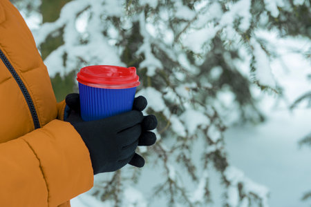 Arms holding a Coffee, paper cup. hands holding a disposable cup on the snowy background. coffee to go in winter concept. Hot and warming drinks in winter concept.の写真素材