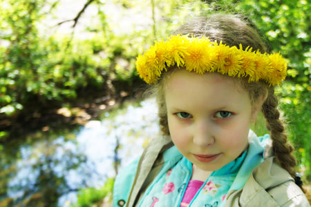 Portrait of a beautiful girl in spring. Child on the background of spring trees. The girl in a wreath of yellow dandelions. Spring conceptの写真素材