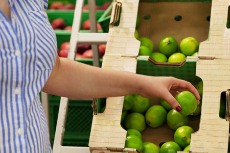 The female hand takes yellow, green fruits in a supermarket close-up. girl holding lime. The concept...