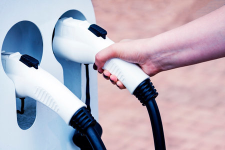 The female hand takes an electric vehicle charging cable. The driver picks up a cable to charge the...