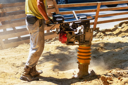 Construction worker compacting soil in house foundation using compactor. Work with tamping machine!...