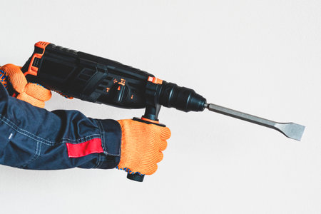workman with a rotary hammer. Hands in protective gloves with hammer drill perforator. Copy space.の写真素材
