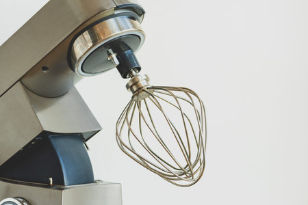 Side view of a modern silver kitchen stand mixer with a metal whisk head, ready for baking and food...
