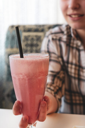 A bright and sunny photo of a hand holding a glass of pink fruity drink, symbolizing summer vacation and relaxation.の写真素材