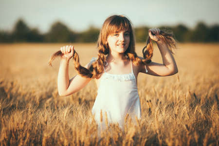Beauty Girl Outdoors enjoying nature, raising hands. Beautiful Teenage Model girl with long healthy blowing hair running on the Spring Field, Sun Light Glow Sun. Free Happy Woman. Toned in warm colorsの写真素材
