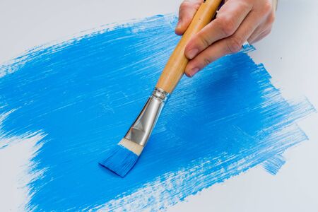 Hobby artist painting with blue acrylic paint on white foam boardの写真素材