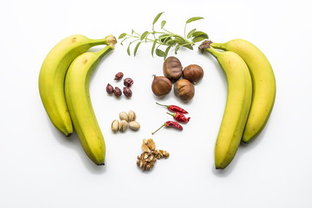 Various fruits flat layed on white background. Bananas, pistachio, sage, hip and chilly pepper. Healthy fruits.の写真素材