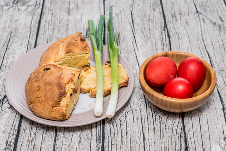 Red Easter eggs in a bamboo bowl with spring onion and sweet easter bread. Istrian Pinca bread. Red eggs are traditionally important during the observation of Orthodox Easter. Served on a table with wooden pattern as a background.の写真素材