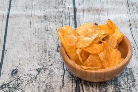 Handful of crisps (or chips) in a bamboo bowl on a wooden background.の写真素材