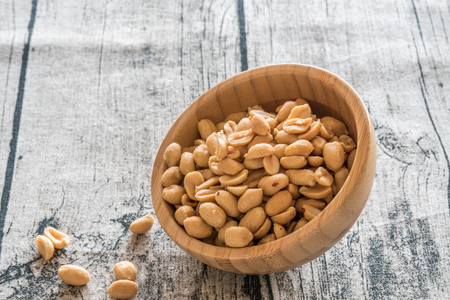 Handful of peanuts in a bamboo bowl on a wooden background.