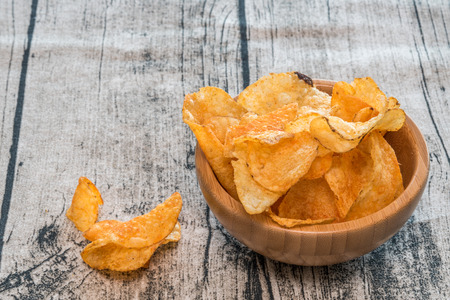 Handful of crisps (or chips) in a bamboo bowl on a wooden background.の写真素材