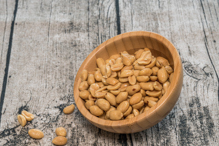 Handful of peanuts in a bamboo bowl on a wooden background.の写真素材