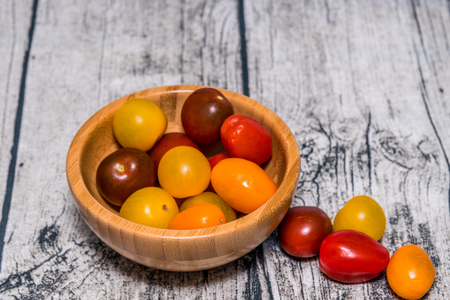 A number of various coloured cherry tomatoes in a bamboo bowl on a wooden background.の写真素材
