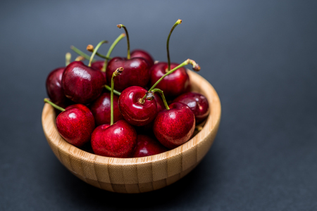 A heap of fresh cherries in a bamboo bowl on a dark backgroundの写真素材