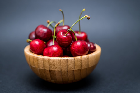 A heap of fresh cherries in a bamboo bowl on a dark backgroundの写真素材