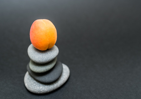 A pile of pebble stones stacked on a black background with an apricot on topの写真素材