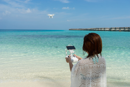 woman with remote controller, controls a flying drone at the sea