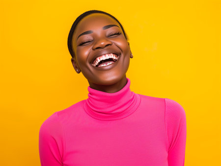 Happy african american woman in pink sweater on yellow background.の素材
