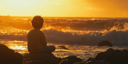 Silhouetted figure sitting in a contemplative pose on rocky coastal cliffs surrounded by a breathtaking sunset over the ocean  This serene and peaceful scene evokes a sense of solitude tranquilityの素材