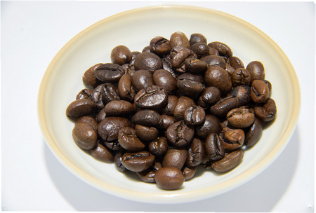 coffee beans and shadow in little bowl on white backgroundの写真素材