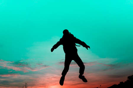 Silhouette man jump of sunset sky. Color scheme is like another world of mystery, like a person...