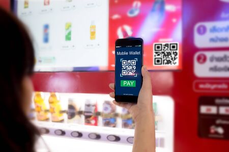 Mobile wallet concept.Woman hands scaning QR code via mobile phone with Smart Vending machine as backgroundの写真素材