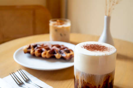 A Sunday morning meal in cafe, two cups of coffee, honey latte and Eispanner americano served with waffle on plate, decorated with with vase.の写真素材