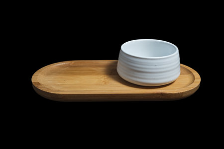 Isolated Ceramic mug of tea, made of white clay, on a wooden plate on black background.の写真素材