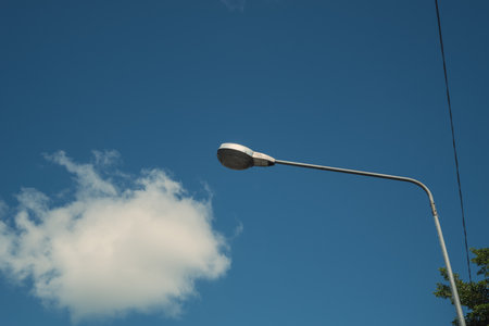Modern electricity lamp post with blue sky and cloud as background. Steel street light or lantern on pole in the daytime are conceptualized in industrial, technological, and urbanize.の写真素材