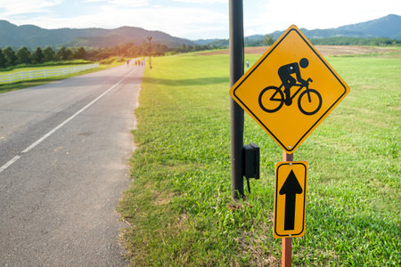 Scenic of country roadside with yellow bicycle lane sign and massive green grass field. Share the road with cyclists bike riding trail warning road sign concept.の写真素材