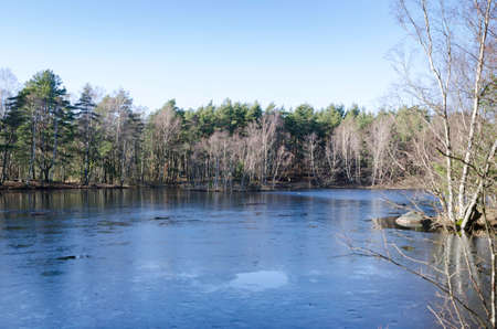 one little lake in Februari the water is still and frozen and the sky is blueの写真素材