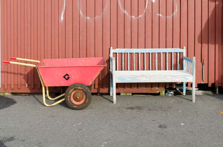 empty rusty weelbarrow between the bench and the red wall as backgrounの写真素材