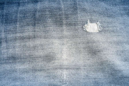 old blue jeans textiles background with a hole and threads