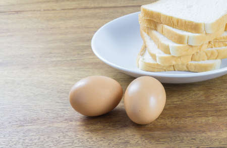 eggs and sliced of bread in white plate, food on wood tableの写真素材