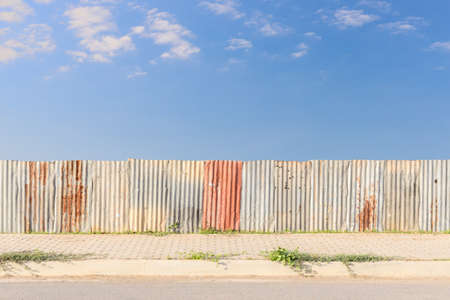 galvanized sheet fence and footpath beside asphaltic road with blue sky backgroundの写真素材