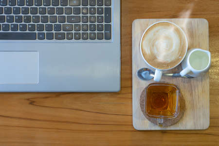 hot coffee with tea and laptop on wood table, work place, selective focusの写真素材