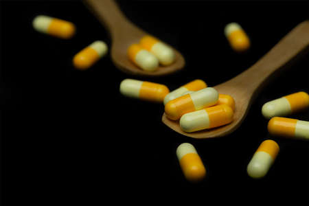 yellow pill capsules on wood spoon isolated on black background, dark tone