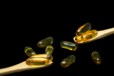 yellow fish oil capsule on wood spoon isolated on black background