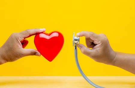 hand holding red heart and stethoscope on yellow  background, medical and health care concept