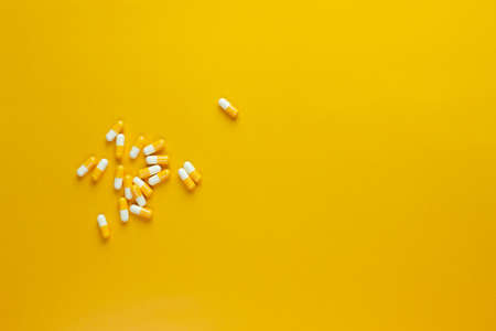 hand picked and holding yellow pill capsule on yellow background, medication concept with copy spaceの写真素材
