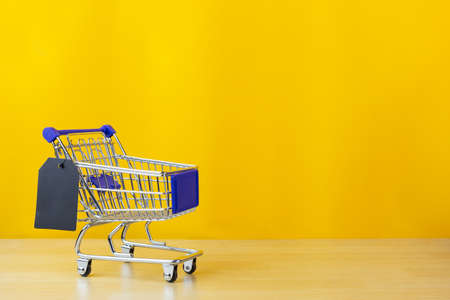 shopping cart toy with black tags label on wood floor  and yellow backgroundの写真素材