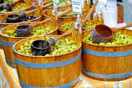 Green olives in wooden buckets sold on market の写真素材