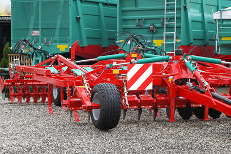 Red disc harrow and green trailers at farm