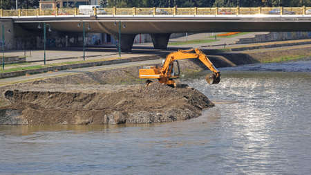 Excavator Machine Digging Levee at River Embankmentの写真素材