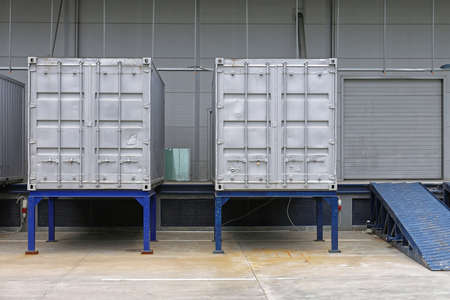 Two Shipping Containers With Leg Support in Front of Warehouse