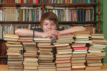 Young Teenage Boy at Big Pile of Books in Library