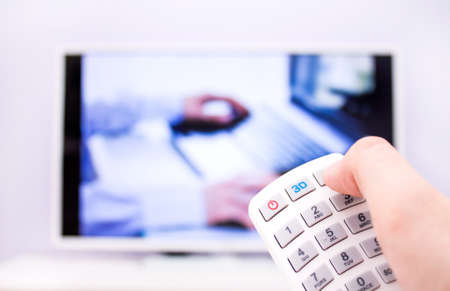 Man presses the 3D button on the remote control. White TV on background.