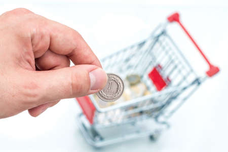 Male hand throws a coin into money box of the shape of trolley. The conception of how to cost-effective spend money while shoppinの写真素材