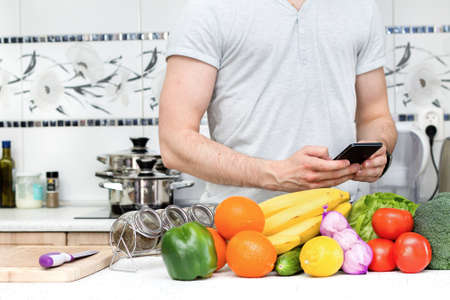 Using smartphone in the kitchen by healthy manの写真素材